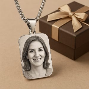 پلاک نقره‌ای مستطیلی با حکاکی دقیق چهره یک زن خندان، قرارگرفته در کنار جعبه کادویی شیک با روبان طلایی – نمادی از هدیه‌ای خاص و ماندگار برای عزیزان.